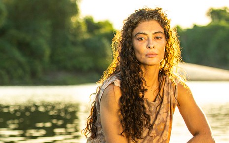 A atriz Juliana Paes, sentada em um tronco dentro do rio, e caracterizada como Maria Marruá em Pantanal