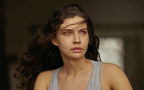 Alanis Guillen em cena de Pantanal: atriz está com os cabelos soltos, regata cinza clara e olha para o lado direito