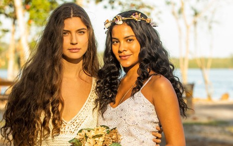 Alanis Guillen, caracterizada como Juma, usa um vestido de noiva e tem o semblante sério; Bella Campos, também vestida de noiva, dá um leve sorriso para a câmera em ensaio de divulgação de Pantanal