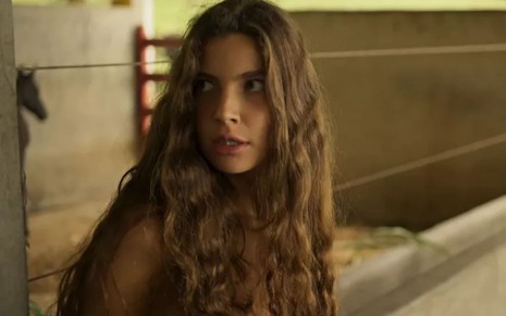 Alanis Guillen, caracterizada como Juma em Pantanal; atriz tem o rosto com manchas de sol, boca seca e cabelos castanhos soltos. Ela encara um ponto fixo com o canto dos olhos, os dentes inferiores à mostra, em cena de Pantanal