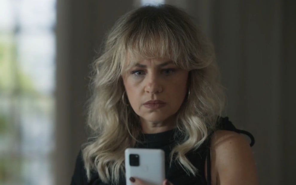 A atriz Karine Teles olha para celular com expressão brava em cena de Pantanal como Madeleine