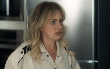 Madeleine (Karine Teles) está ao lado de geladeira e aparenta irritação em seu rosto