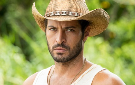 Leandro Lima caracterizado como Levi: ele usa um chapéu de palha e uma regata branca. O semblante expressa ódio em ensaio de divulgação de Pantanal
