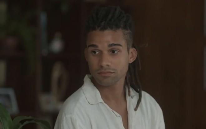 Marcelo (Lucas Leto) está sentado em sofá na sala de sua casa em cena de Pantanal, novela das nove da Globo