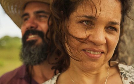 Isabel Teixeira, caracterizada como Maria Bruaca, tem a expressão provocante; ao fundo, é possível ver Juliano Cazarré, o Alcides, dando um leve sorriso em cena de Pantanal