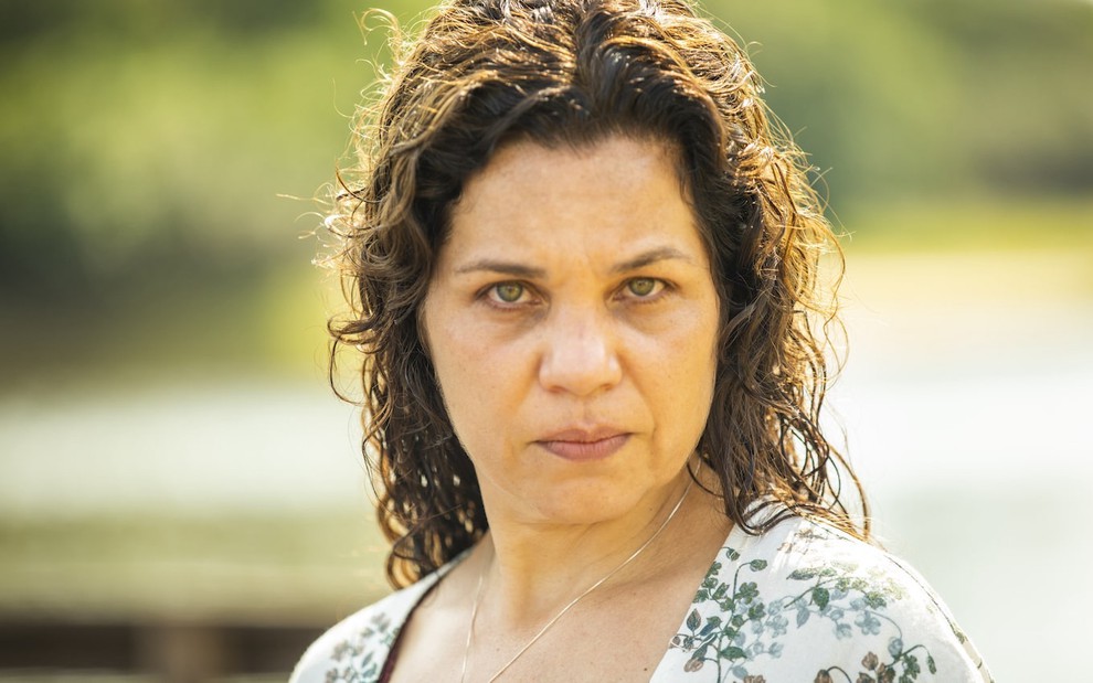 A atriz Isabel Teixeira está à beira de um rio e olha para frente com seriedade caracterizada como Maria Bruaca, sua personagem em Pantanal