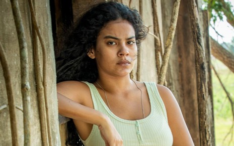 Bella Campos em cena de Pantanal: atriz está com braço apoiado em janela e olha para frente