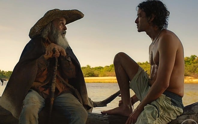 Osmar Prado e Jesuita Barbosa, como seus personagens em Pantanal, estão conversando sentados em um tronco de árvore