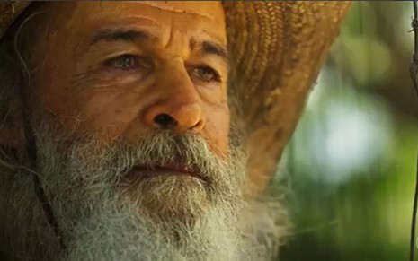 Osmar Prado usa chapéu e barba comprida, caracterizado como Velho do Rio em cena de Pantanal, novela das nove da Globo