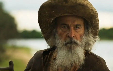 Osmar Prado caracterizado como Velho do Rio. Ele usa o cabelo e a barba longas, e veste chapéu de palha e casaco de couro.