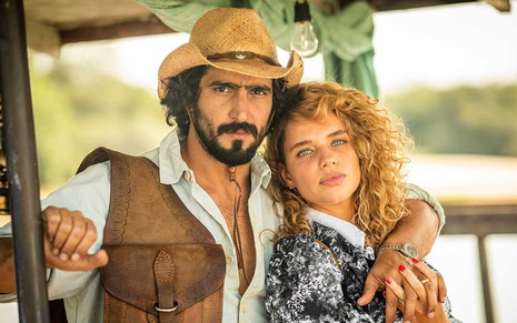 O ator Renato Góes como José Leôncio abraça Bruna Linzmeyer, a Madeleine, em um barco no meio do rio em cena de Pantanal