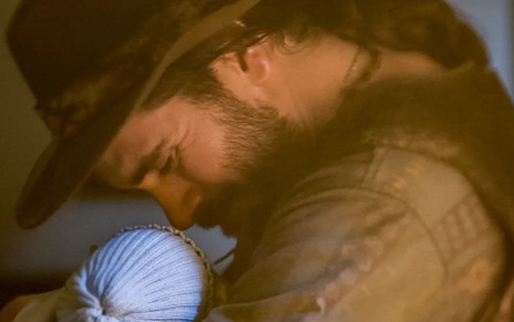 Gabriel Sater, caracterizado como Trindade, dá um sorriso emocionado enquanto encosta o rosto em um bebê em Pantanal