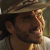 O ator e cantor Gabriel Sater sorri de maneira sinistra em cena de Pantanal na qual usa um chapéu e está caracterizado como Trindade