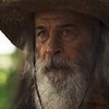 O ator Osmar Prado segura cajado e usa um chapéu em cena de Pantanal na qual está caracterizado como o Velho do Rio