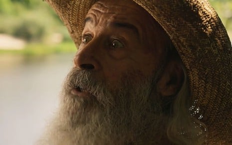 Osmar Prado caracterizado como Velho do Rio. Ele usa o cabelo e a barba longas e veste chapéu de palha e casaco de couro.