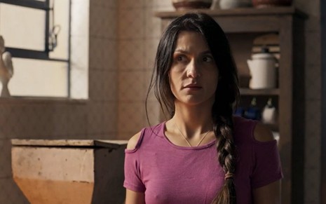 A atriz Paula Barbosa usa uma blusa roxa e está com uma trança lateral nos cabelos em cena de Pantanal, novela das nove da Globo