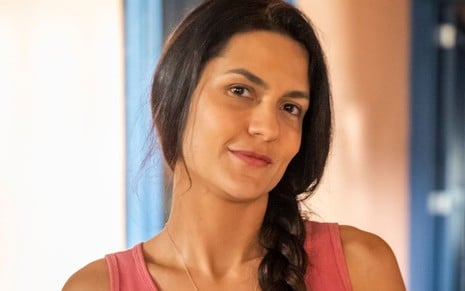 Paula Barbosa caracterizada como Zefa em Pantanal: atriz tem os cabelos longos, lisos e escuros. Ela veste uma regata surrada e encara a câmera com um leve sorriso em ensaio de divulgação de Pantanal