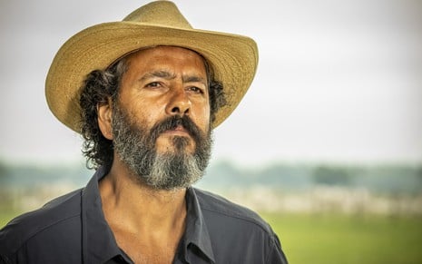 O ator Marcos Palmeira está com barba grande e usa chapéu e camisa escura em cena de Pantanal, novela das nove da Globo