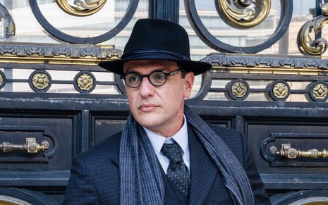 Rodrigo Lombardi como o escritor João Guimarães Rosa em cena de Passaporte para Liberdade: ator usa óculos, terno preto, cachecol e chapéu