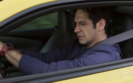 João Baldasserini grava de camiseta de manga longa azul, dirigindo carro amarelo e chorando como Agnaldo de Pega Pega