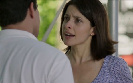 Cíntia (Bruna Spínola) está em pé e de cabelo solto, ela conversa com Júlio (Thiago Martins), que está de costas em cena de Pega Pega