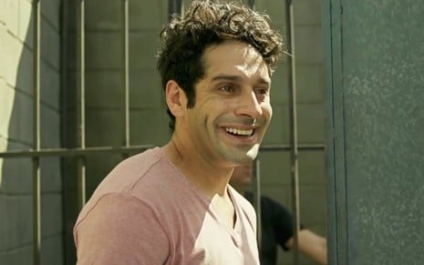 Agnaldo (João Baldasserini) sorri parado em frente ao portão do presídio em cena de Pega Pega
