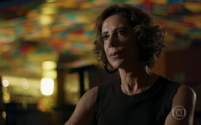 Angela Vieira grava com vestido preto, cabelo curto e expressão séria como Lígia de Pega Pega, reprise da Globo