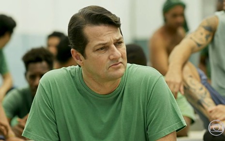 Marcelo Serrado grava cena com expressão triste, com uniforme de presídio verde, como Malagueta em Pega Pega