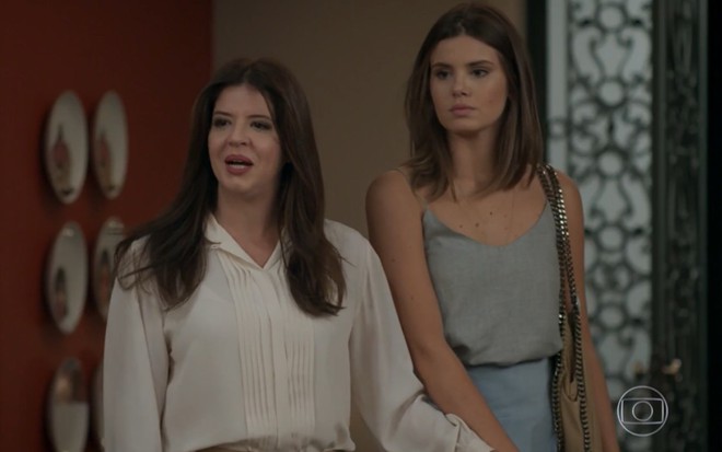 Mariana Santos grava com camisa branca e batom vermelho de mãos dadas com Camila Queiroz, como Maria Pia e Luiza de Pega Pega