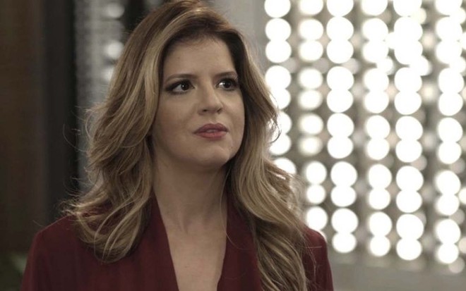A atriz Mariana Santos caracterizada como Maria Pia, com um vestido vermelho e cabelos loiros, em cena de Pega Pega