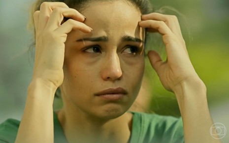 Sandra Helena (Nanda Costa) veste uniforme verde de presidiária e está com o cabelo preso; ela chora e coloca as duas mãos no rosto em cena de Pega Pega