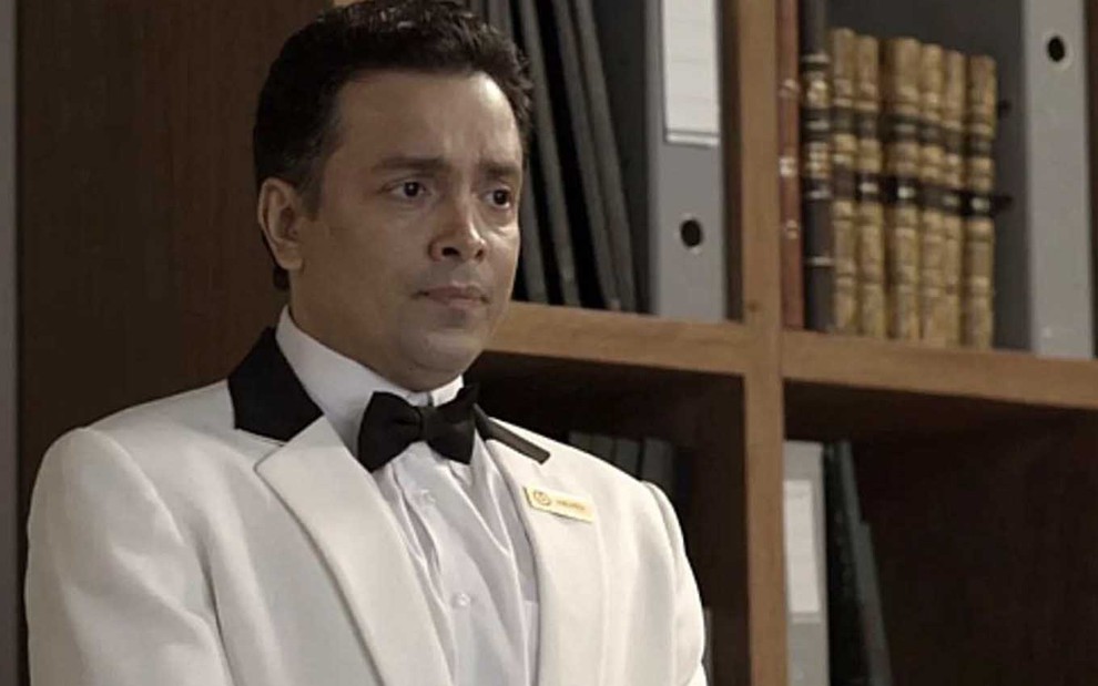 O ator Rodrigo Fagundes está vestido com um summer, com gravata borboleta preta, como o Nelito em cena de Pega Pega