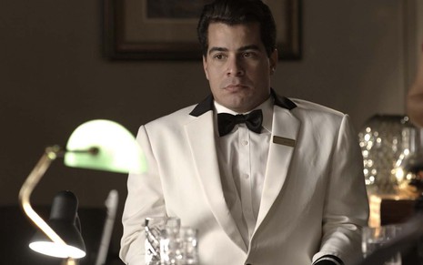 O ator Thiago Martins está com um summer de garçom com uma gravata borboleta branca como o Júlio em cena de Pega Pega