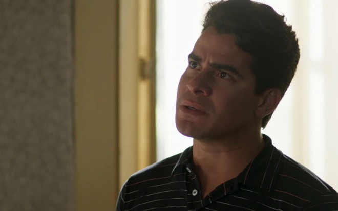 Júlio (Thiago Martins) está em pé na sala de sua casa e aparenta estar com raiva em cena de Pega Pega