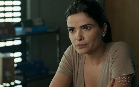 Antônia (Vanessa Giácomo) está sentada na mesa do escritório de Siqueira (Marcelo Escorel) na delegacia em cena de Pega Pega
