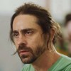 Felipe Abib, caracterizado como Roni, tem a expressão perturbada em Quanto Mais Vida, Melhor!; ator tem os cabelos presos e usa uma blusa verde