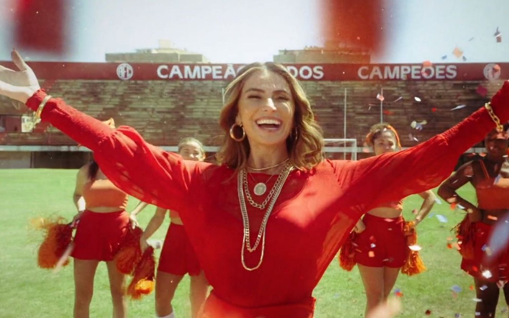 Paula Terrare (Giovanna Antonelli) está em campo de futebol com líderes de torcida em cena de Quanto Mais Vida, Melhor!