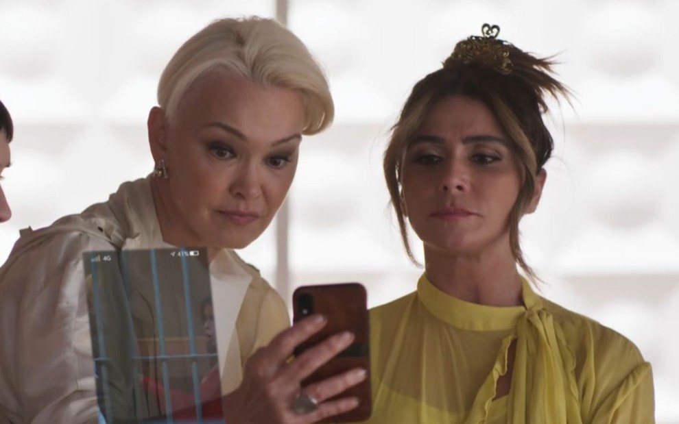 Julia Lemmertz grava cena olhando para um celular, ao lado de Giovanna Antonelli, como Carmem e Paula
