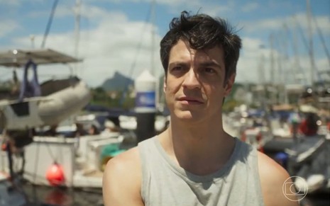 Flávia/Guilherme (Mateus Solano) está parado em marina de barcos em cena de Quanto Mais Vida, Melhor!