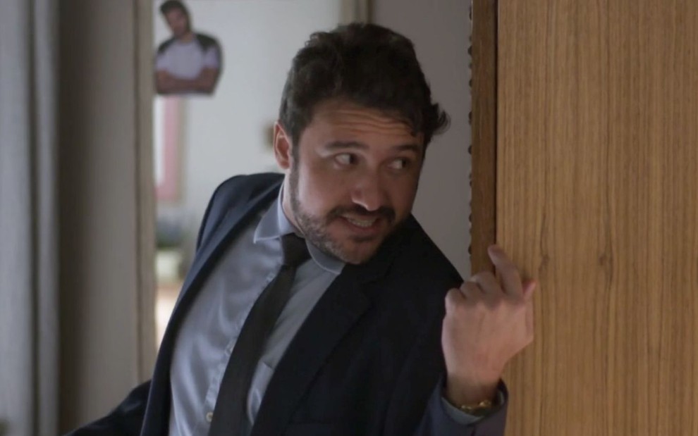Thardelly Lima em cena de Quanto Mais Vida, Melhor: caracterizado como Odaílson, ator está de terno, gravata e olha para alguém fora do quadro