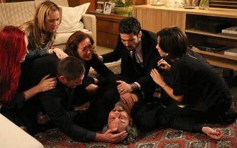 O ator Alexandre Nero, desmaiado no chão, em cena como José Alfredo em Império; ele está cercado por outros atores, que choram