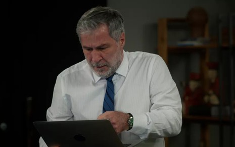 O ator Leopoldo Pacheco, com um laptop na mão, em cena como Hugo em Salve-se Quem Puder