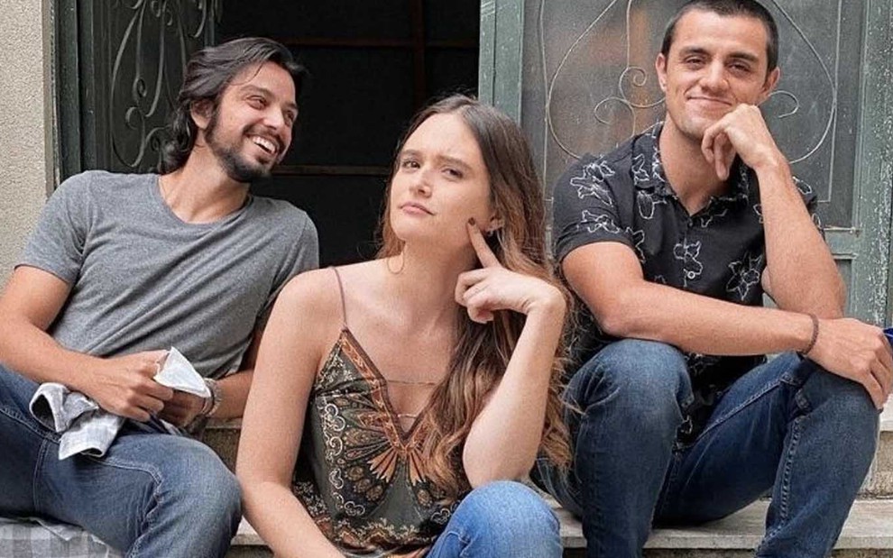 O ator Rodrigo Simas à esquerda, com Juliana Paiva no centro e Felipe Simas à direita, eles estão sentados em uma escada na porta de uma igreja durante uma pausa nas gravações de Salve-se Quem Puder