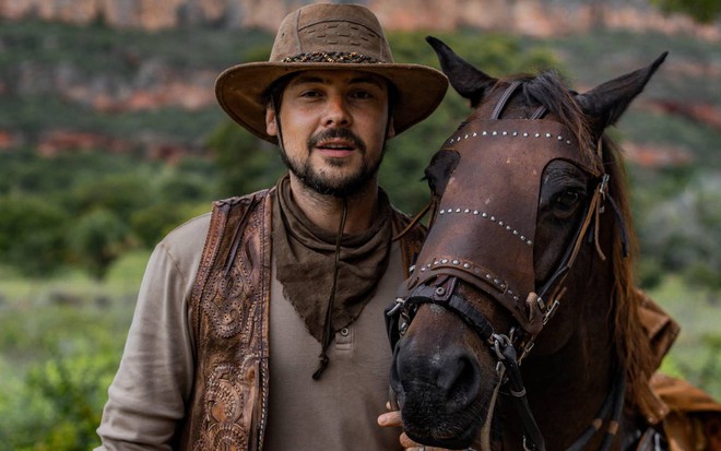 Ator Sergio Guizé surge ao lado de cavalo e olha para a câmera
