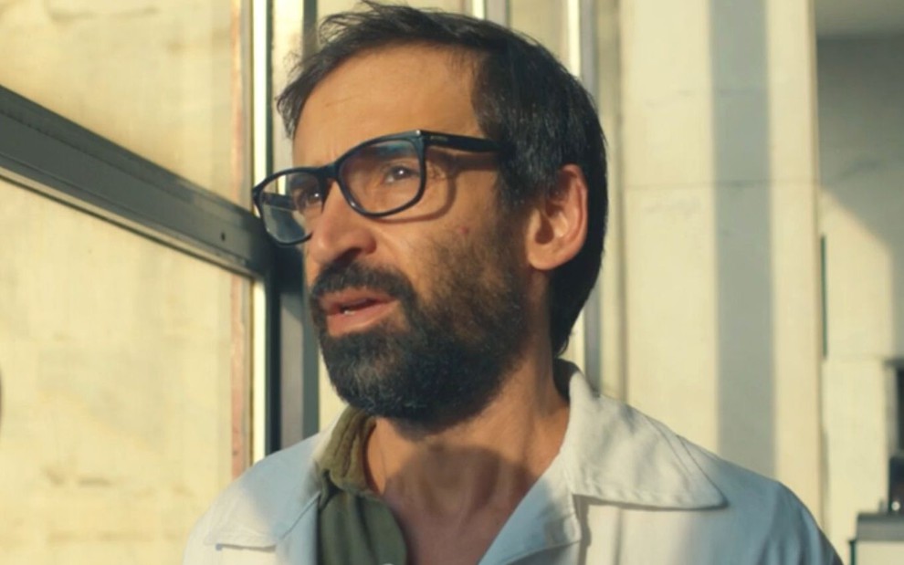 O ator Julio Andrade olha por uma janela como o personagem Evandro em cena da série Sob Pressão