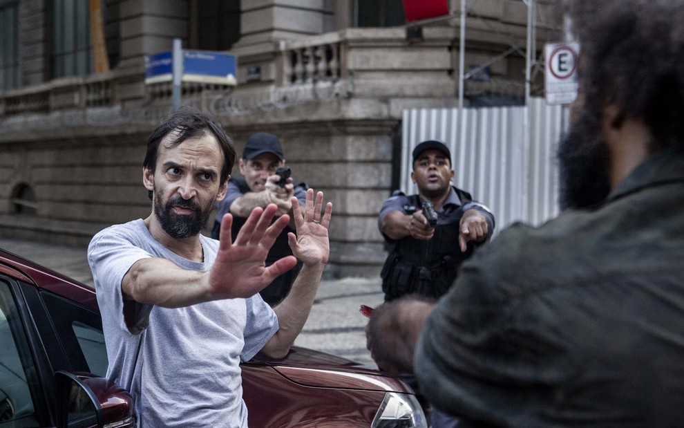 O ator Julio Andrade grava cena de Sob Pressão em rua do Rio de Janeiro com figurantes usando farda de polícia atrás dele