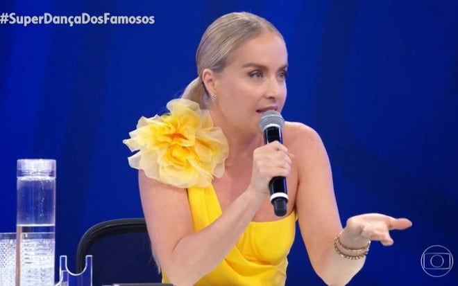 De vestido amarelo com um grande enfeito no ombro, Angélica tem expressão séria no júri da Super Dança dos Famosos