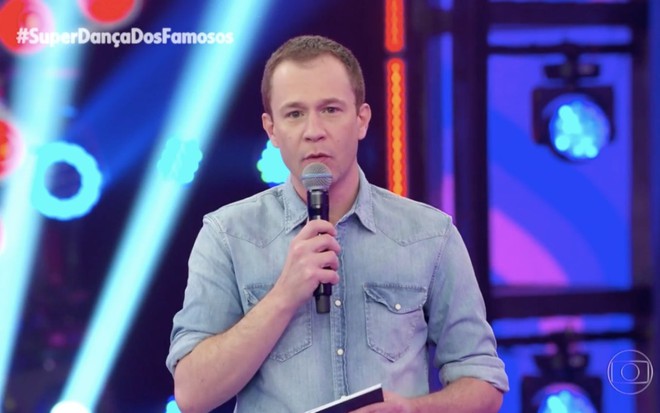 Tiago Leifert apresentando a Super Dança dos Famosos no domingo (18); ele usa camisa jeans e segura um microfone