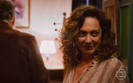A atriz Eliane Giardini em cena de Terra e Paixão como Agatha sorri disfarçadamente enquanto Tony Ramos, o Antônio, está de costas