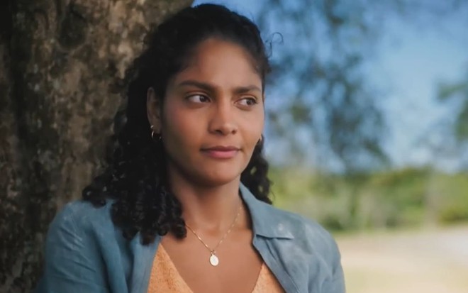 Barbara Reis caracterizada como Aline; ela usa uma camiseta verde e tem o semblante abalado em cena de Terra e Paixão